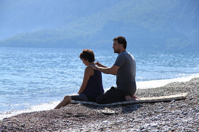 Muž so ženou sedia pri mori, pláž, masáž ramien, relax.jpg